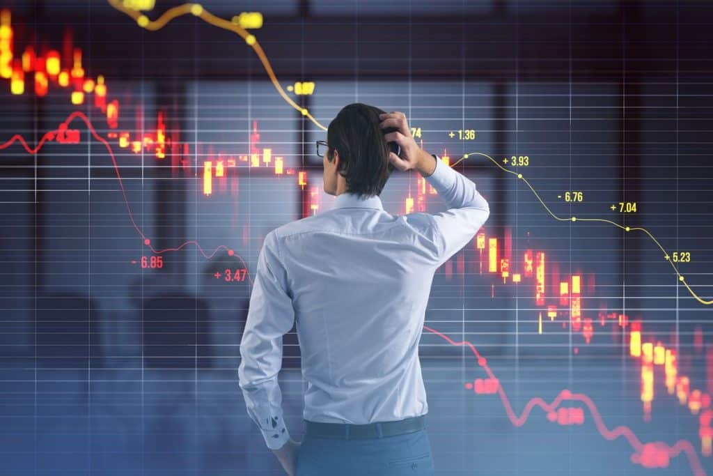 A worried investor looks at falling stock market charts on a digital screen, representing the volatility and risks associated with Index funds during market downturns.
