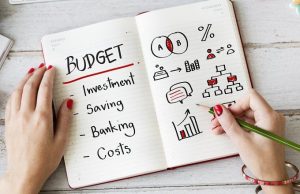 Open notebook with the word “BUDGET” written on one page, listing investment, saving, banking, and costs, while the opposite page shows hand-drawn financial charts and diagrams. The image illustrates the concept of financial planning and organizing money for future goals.