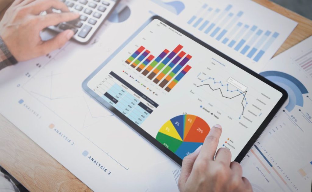 A person uses a tablet displaying colorful charts, bar graphs, and pie charts to analyze financial data, representing the balance between fixed income and variable income in investment strategies.