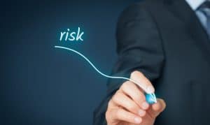 A businessman in a suit draws a downward arrow with the word “risk,” symbolizing the stability and security offered by low-risk investments.