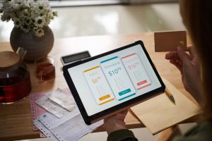 Person holding a credit card while viewing pricing plans on a tablet screen, showing options for Basic, Standard, and Premium services. The image illustrates decision-making and budgeting related to monthly subscriptions.